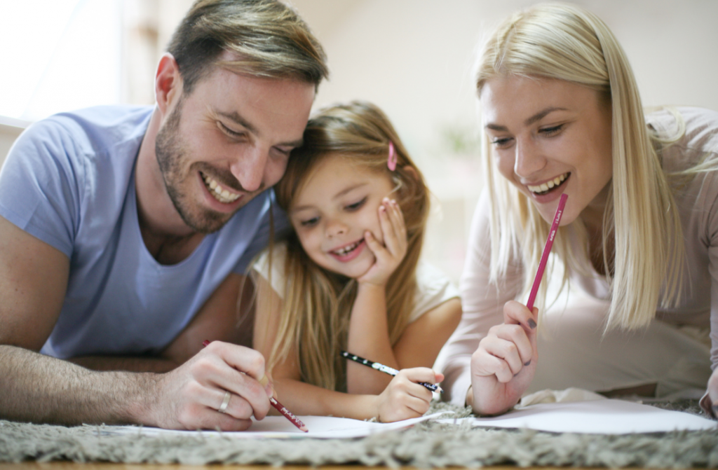 Uśmiechnięci mama i tata uczą córkę podczas edukacji domowej.